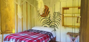 A single bed with a checkered blanket, a wall-mounted plant, and a wooden shelf with towels.