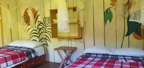 Ein Zimmer mit zwei Betten, einem kleinen Tisch und einer Wand mit Pflanze und Pendelleuchte.