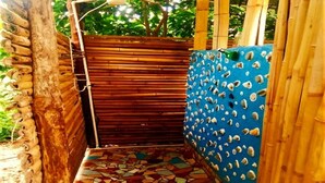 Een smalle buitendouche met betegelde vloer, bamboe wanden en een blauwe wand met gaten.