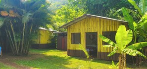 A small, single-story building with a sloped roof, surrounded by lush greenery and banana plants.