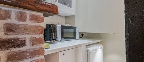 A kitchen with a brick wall, white cabinets, a microwave, and a small refrigerator.