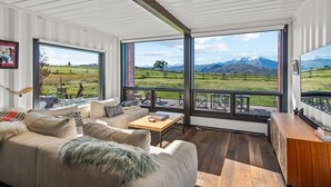 Amplia sala de estar con un ventanal que ofrece vistas a la montaña, un sofá, una mesa de centro y un mueble de madera.