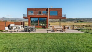 Un edificio moderno de dos pisos con un patio amoblado al aire libre y vistas del paisaje circundante.