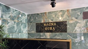 Un espace d’accueil avec un mur en marbre et une enseigne sur laquelle on peut lire « MAGNA OURA ».