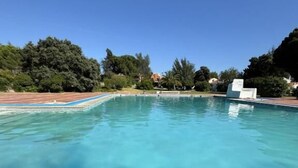 Une piscine d’eau cristalline, entourée d’arbres et bordée d’une terrasse en bois.
