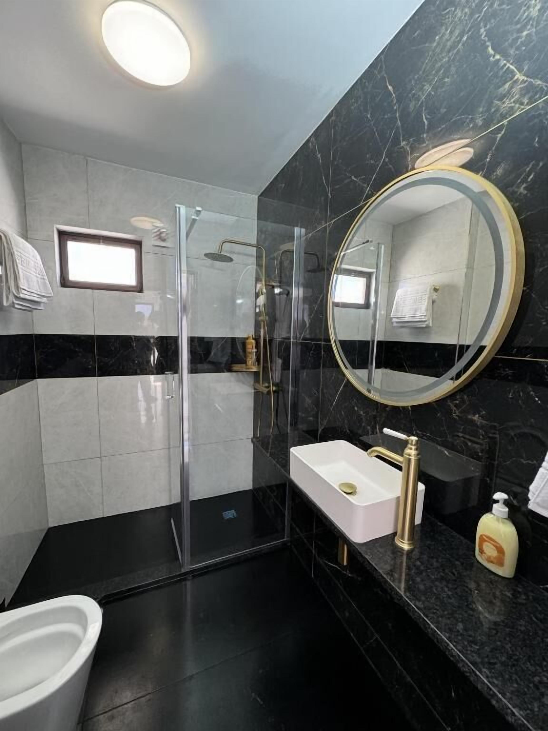 Un bagno moderno con doccia vetrata, un lavandino bianco con rubinetto dorato e uno specchio grande con cornice dorata.