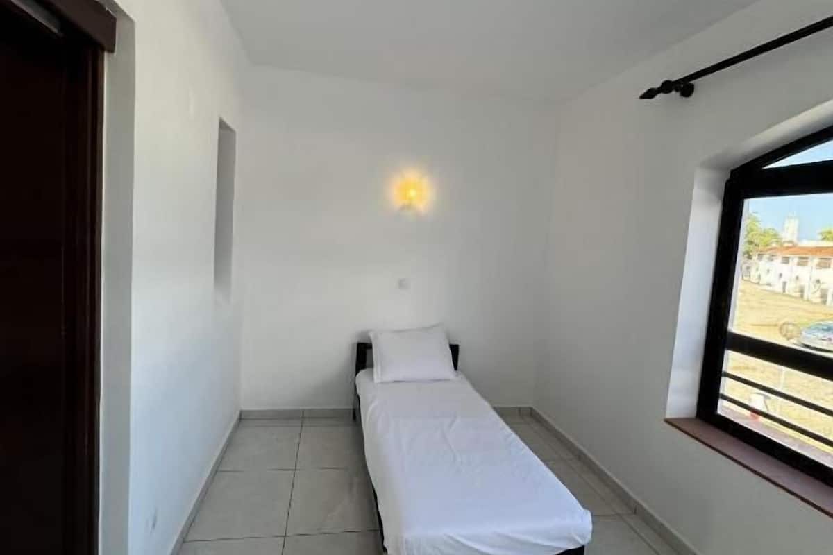 A small, clean room with a single bed, a window with a view, and a ceiling light.