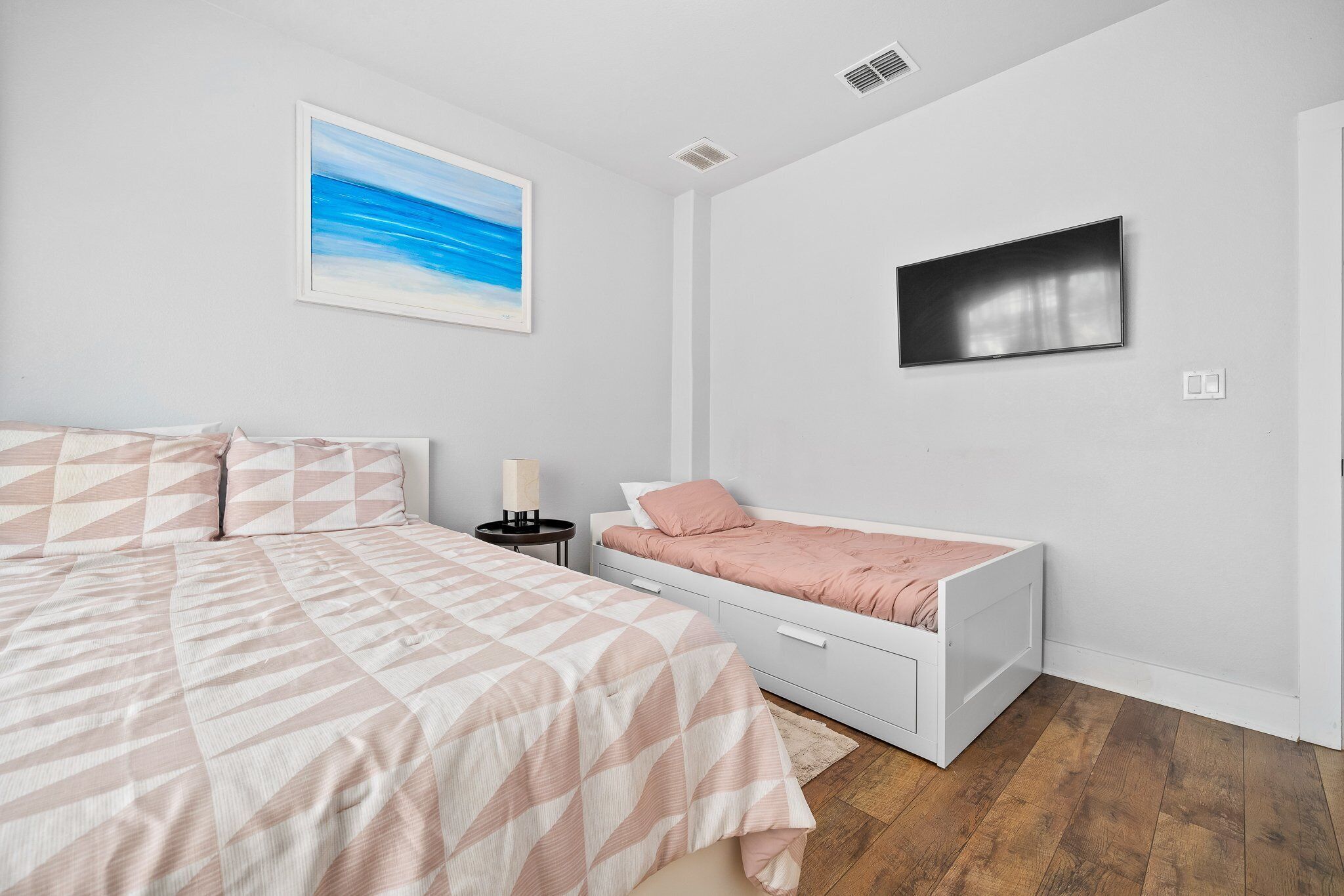 Une chambre à coucher avec un grand lit, un plus petit lit, une table de chevet, une lampe et un tableau au mur.