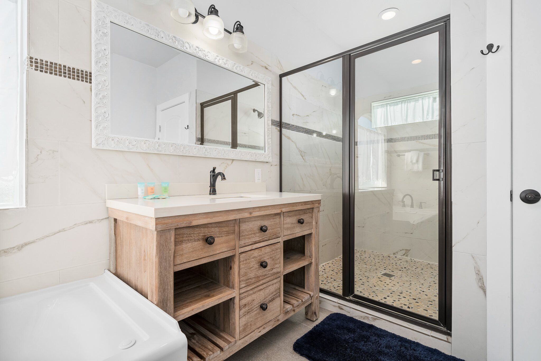 A bathroom with a marble vanity, a large mirror, a glass shower enclosure, and a blue rug.