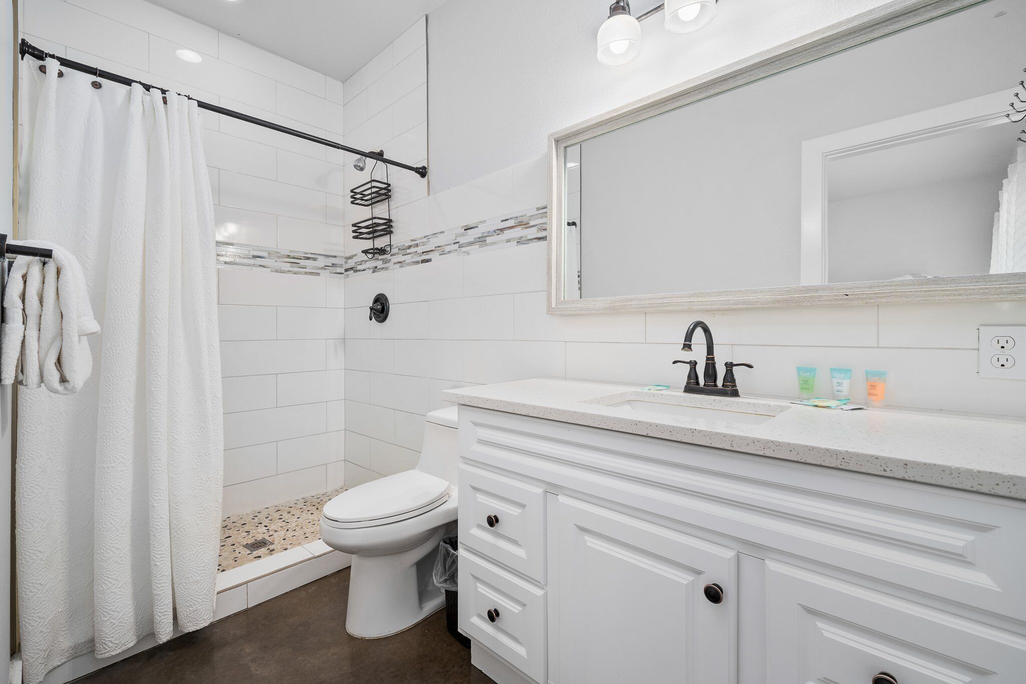 Un baño moderno con ducha, inodoro y tocador con un espejo grande.