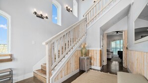 A spacious interior with a wooden staircase, a large window, and a view into another room. - Huge Vacation Home! Community Boardwalk to the Beach (Port Aransas)