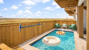 A wooden deck with a pool, outdoor chairs, and a view of the landscape. - St. Jo's Bungalow (Port Aransas)