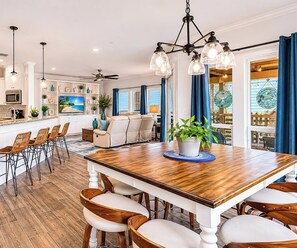 A spacious kitchen with a wooden dining table, bar seating, and a large TV. - Sunrise Paradise - Pet Friendly! Community Pool! (Port Aransas)