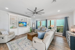 A living room with a sofa, coffee table, TV, and a ceiling fan. - Sunrise Paradise - Pet Friendly! Community Pool! (Port Aransas)