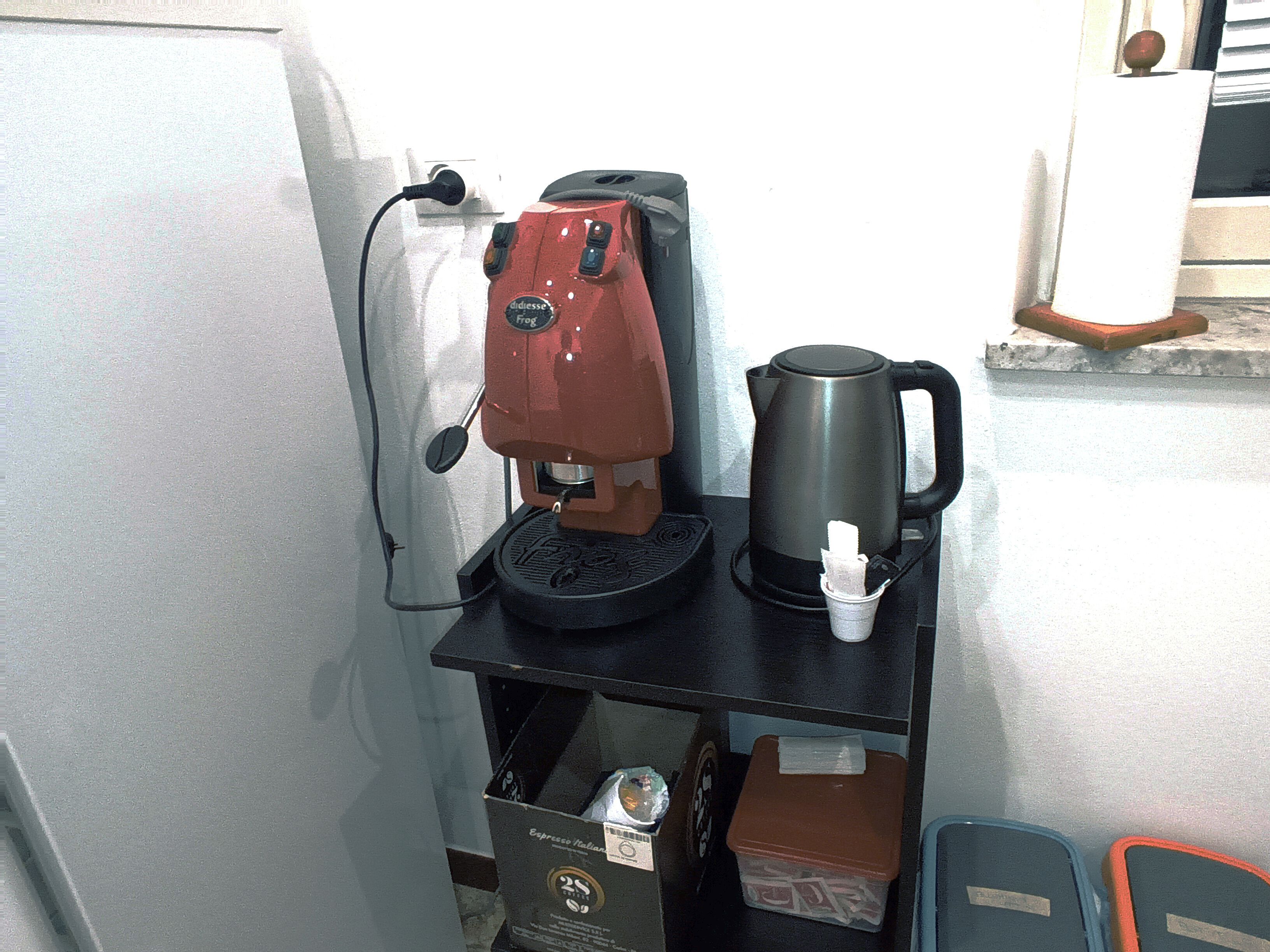 Eine kleine Küchenzeile mit Kaffeemaschine, Wasserkocher und kleinem Mülleimer.