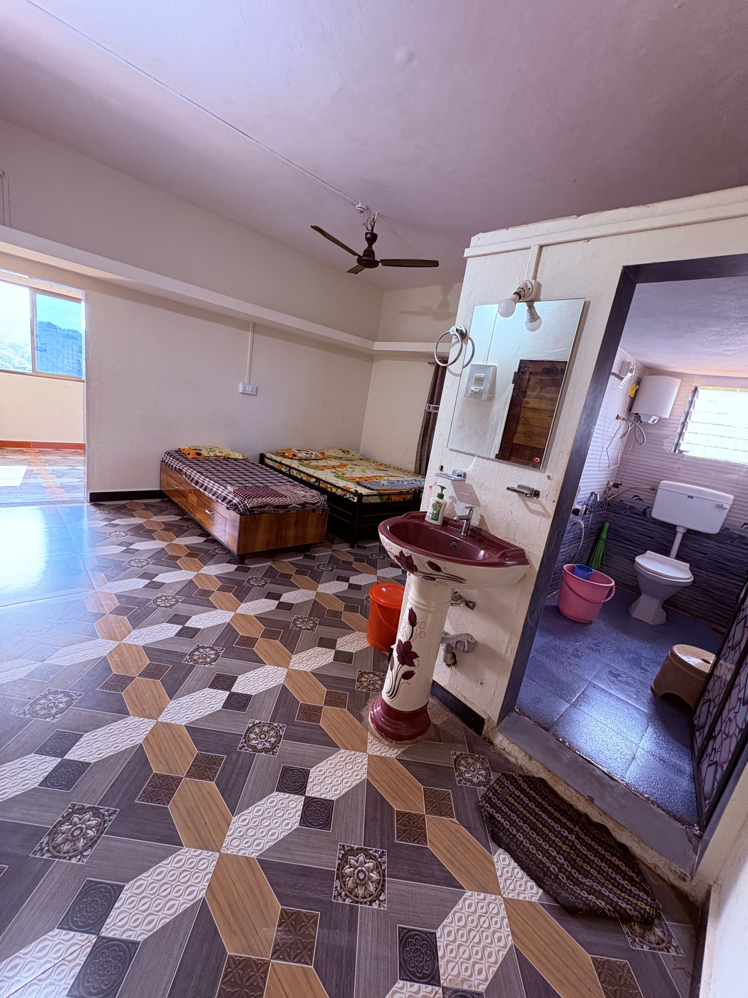 Una habitación con piso estampado, una cama, un ventilador de techo, un lavamanos y vista al baño.