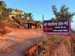 Une enseigne indiquant « Shri Ganapati Home Stay » avec les numéros de téléphone, un chemin de terre, un chien et un bâtiment en arrière-plan.