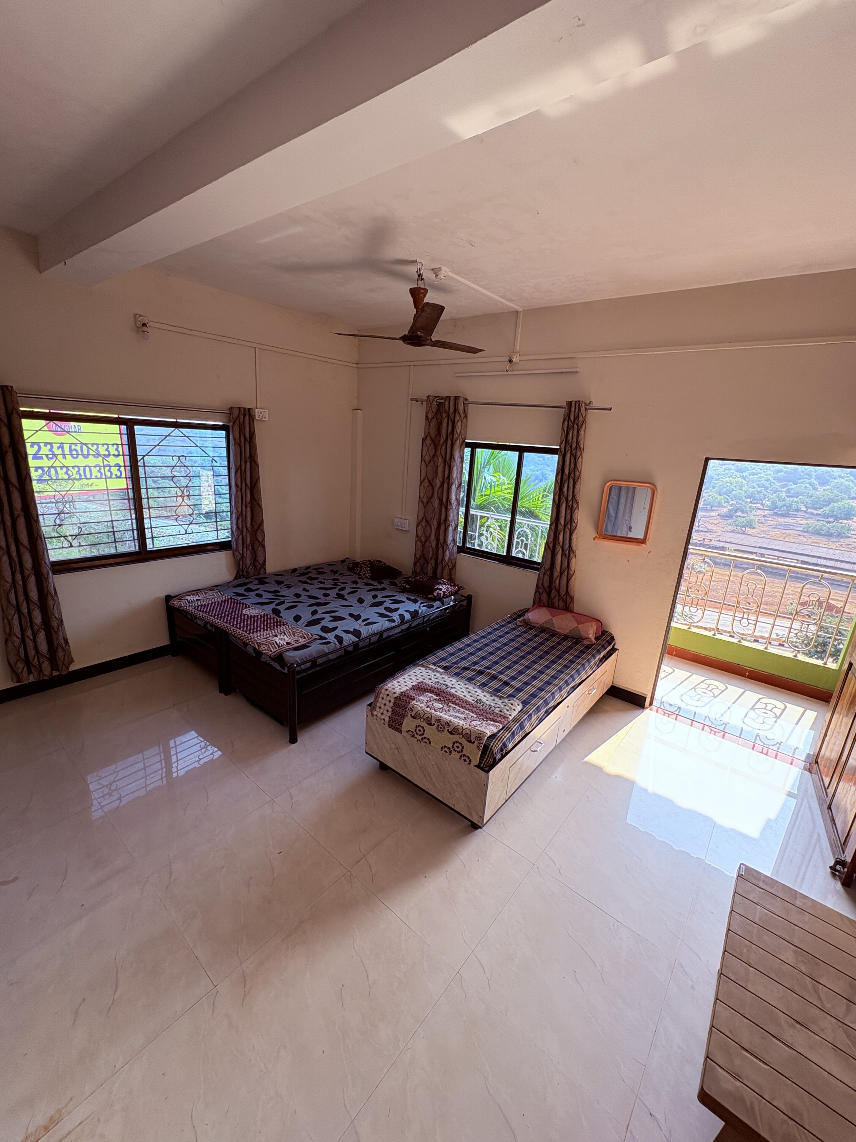 A room with two beds, a ceiling fan, and large windows with curtains.