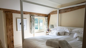 A bedroom with a four-poster bed, a wooden beam ceiling, a window with floral curtains, and a bedside table with a lamp. - Stable Cottage -  a super cottage sleeping 2 guests (Pulborough)