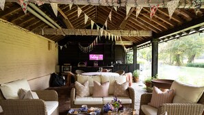 A covered outdoor seating area with wicker furniture, a neon sign, and a view of the garden. - Stable Cottage -  a super cottage sleeping 2 guests (Pulborough)