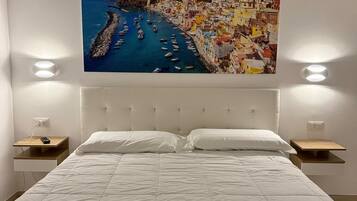 Un dormitorio con una cama grande, ropa de cama blanca, dos mesitas de noche con lámparas y un cuadro de un paisaje urbano sobre la cama.
