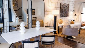 A modern living room with a dining area, featuring a white table, black chairs, and a sofa. There are mirrors, a lamp, and artwork on the walls. - Game day luxury! New! 3 king en suites; 17 min walk to UM; 5 mins to sq; (Oxford)