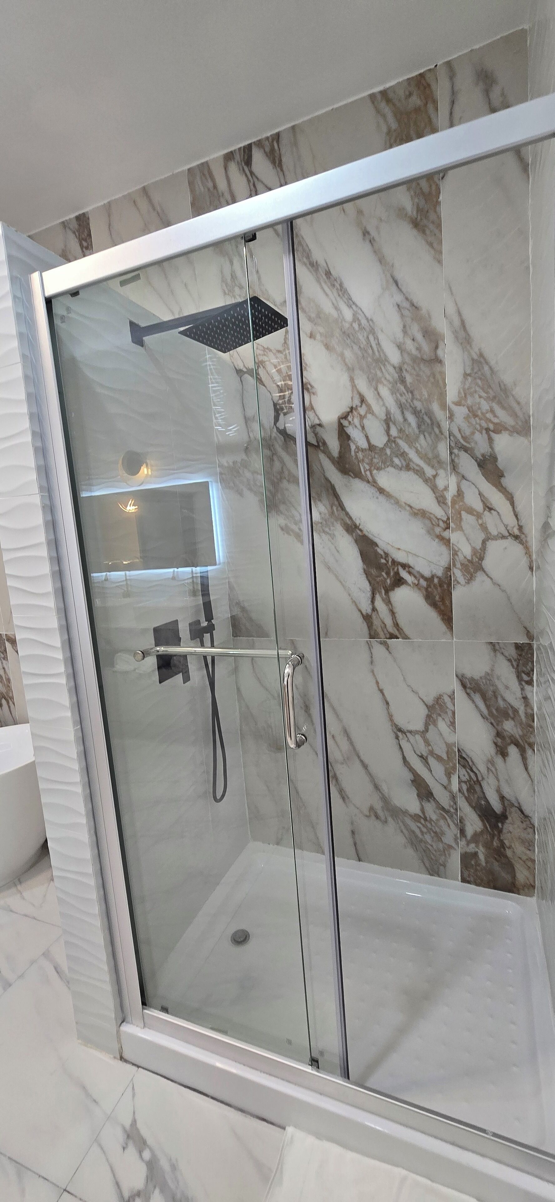 Ducha con cerramiento de vidrio, pared y suelo de mármol, cabezal de ducha manual y grifo monomando.