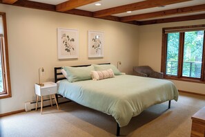Un dormitorio con cama, mesitas de noche, una silla y un cuadro con motivos florales en la pared.