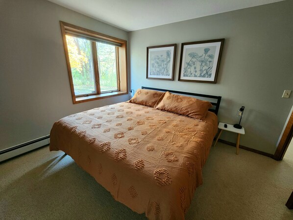 A bedroom with a large bed, a window, and two framed pictures on the wall.