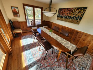 Comedor con una larga mesa de madera, varias sillas, alfombra estampada y un cuadro en la pared.