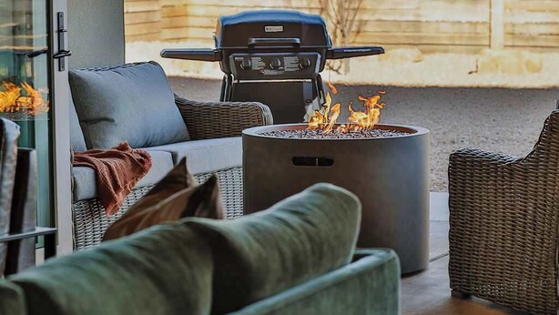 Een terras met een barbecue, vuurkorf en rieten meubilair.