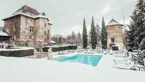 Ein mit Schnee bedeckter Poolbereich mit Liegestühlen und klarem Wasser.