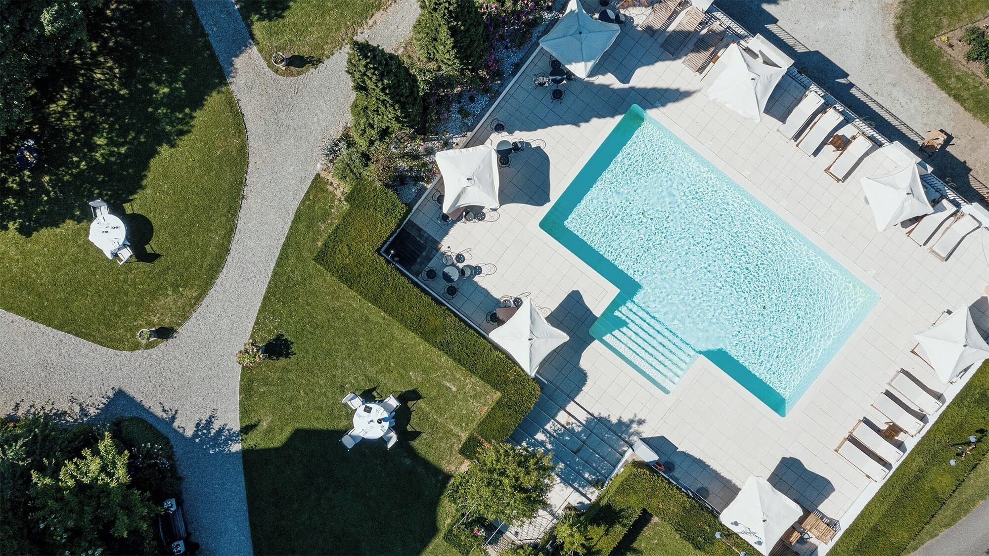 Eine Vogelperspektive auf ein Hotel mit einem großen Schwimmbad, Sitzbereichen im Freien und gepflegten Rasenflächen.