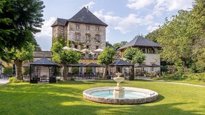 A historic stone building with a tower, surrounded by a well-maintained garden with a fountain, outdoor seating, and umbrellas. - 10 mins de Chambéry ! Chateau, Piscine, Fitness (Chambéry)