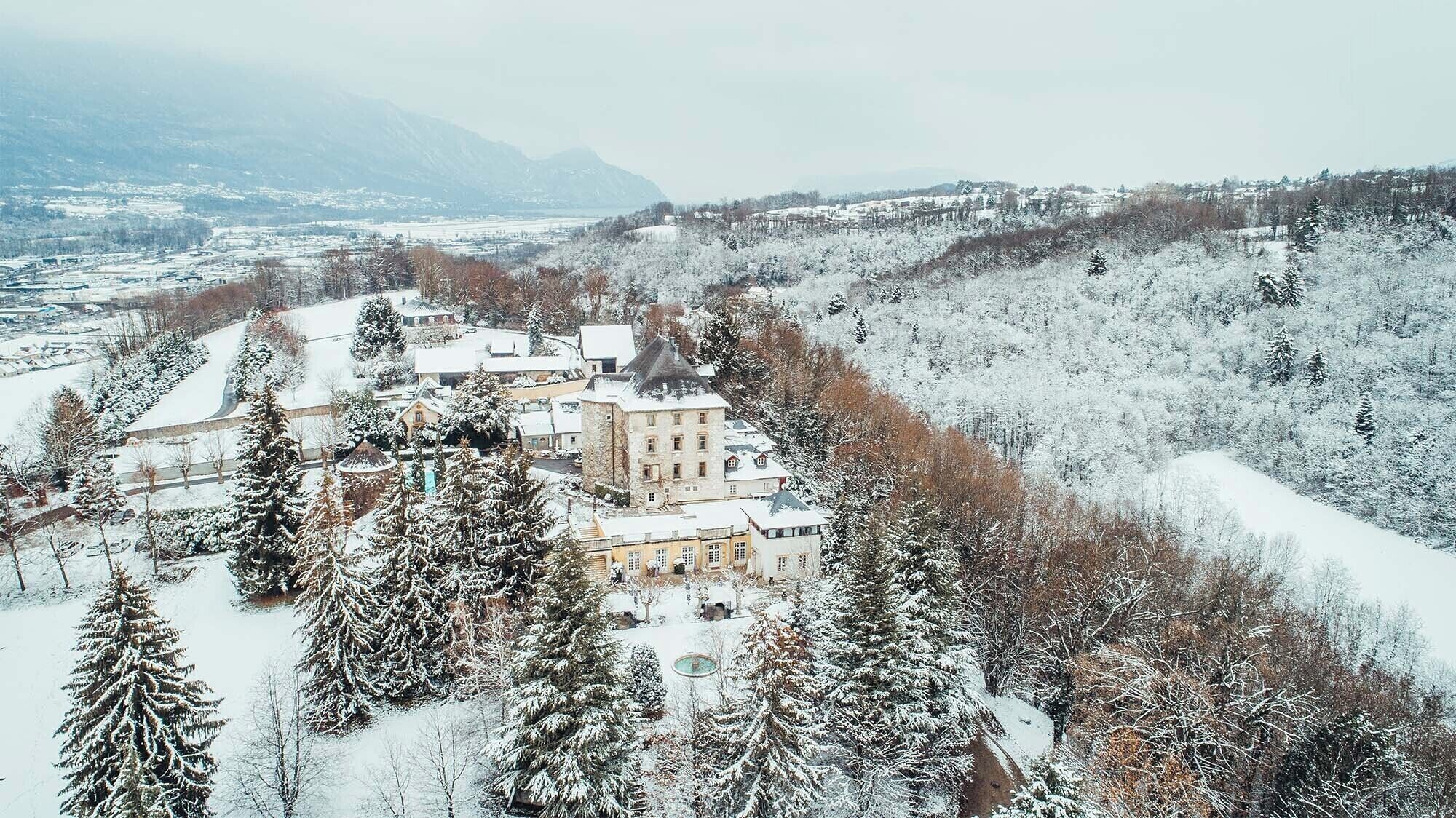 Eine verschneite Landschaft mit einem großen Gebäude, umgeben von Bäumen.