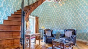 A staircase leading to a landing with a wooden finish, a patterned wallpaper, a chandelier, two leather armchairs, a glass coffee table, and a small table with a lamp. - Chateau Grande Baignoire Double! Vignes + Piscine (Chambéry)