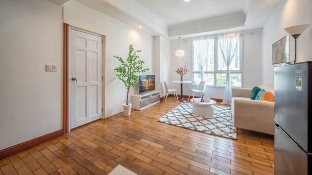 Una sala de estar moderna con suelo de madera, un sofá blanco, una mesa de comedor y un televisor.