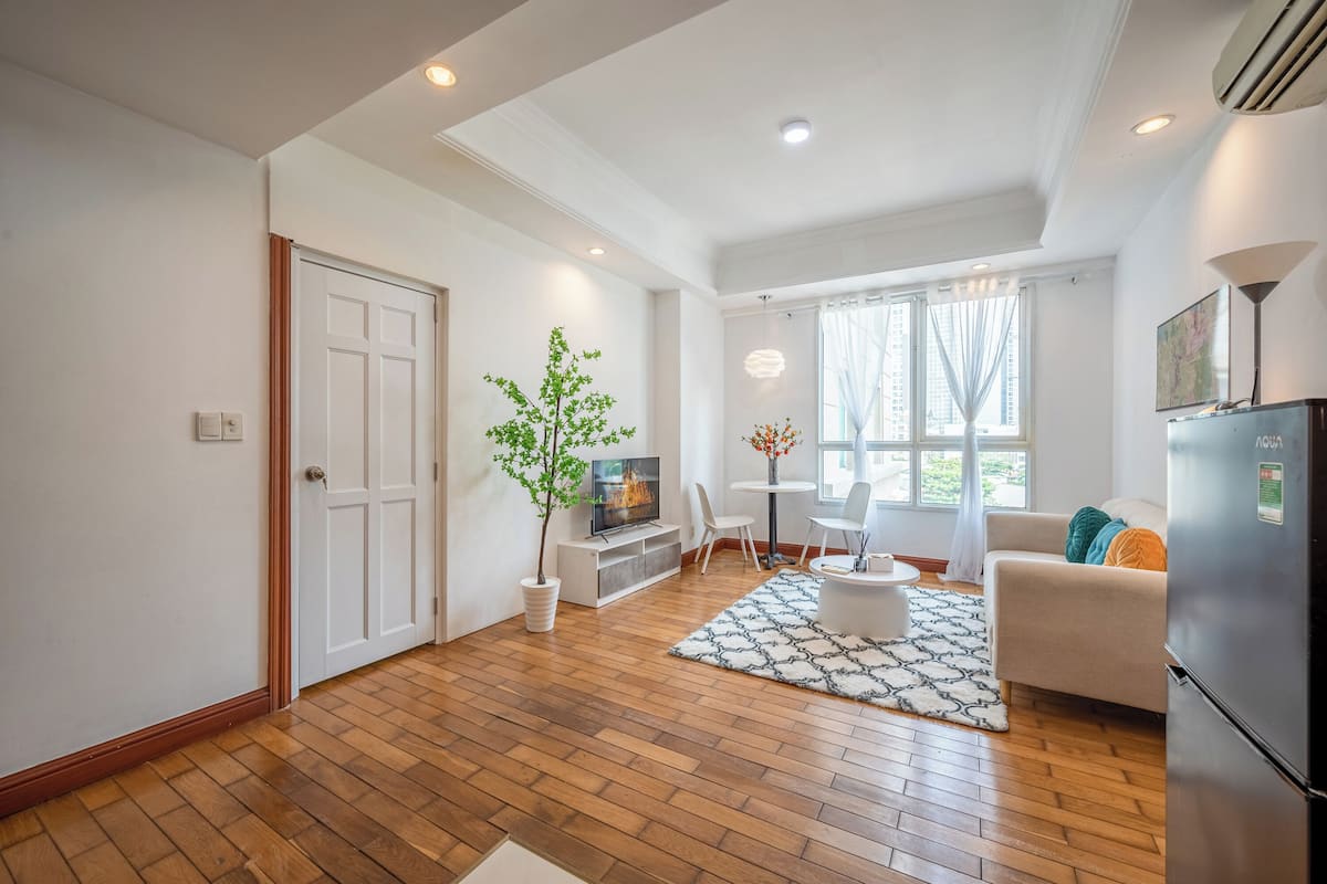 Un salon moderne avec un plancher en bois, un canapé blanc, une table à manger et un téléviseur.