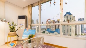 Una habitación con un ventanal grande, un cuadro en la pared, una planta y una silla.