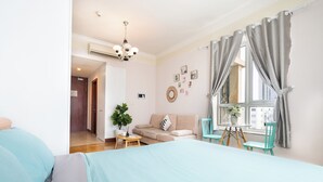 Un dormitorio con cama, ventana con cortinas, sofá, una mesita con planta y vistas al exterior.