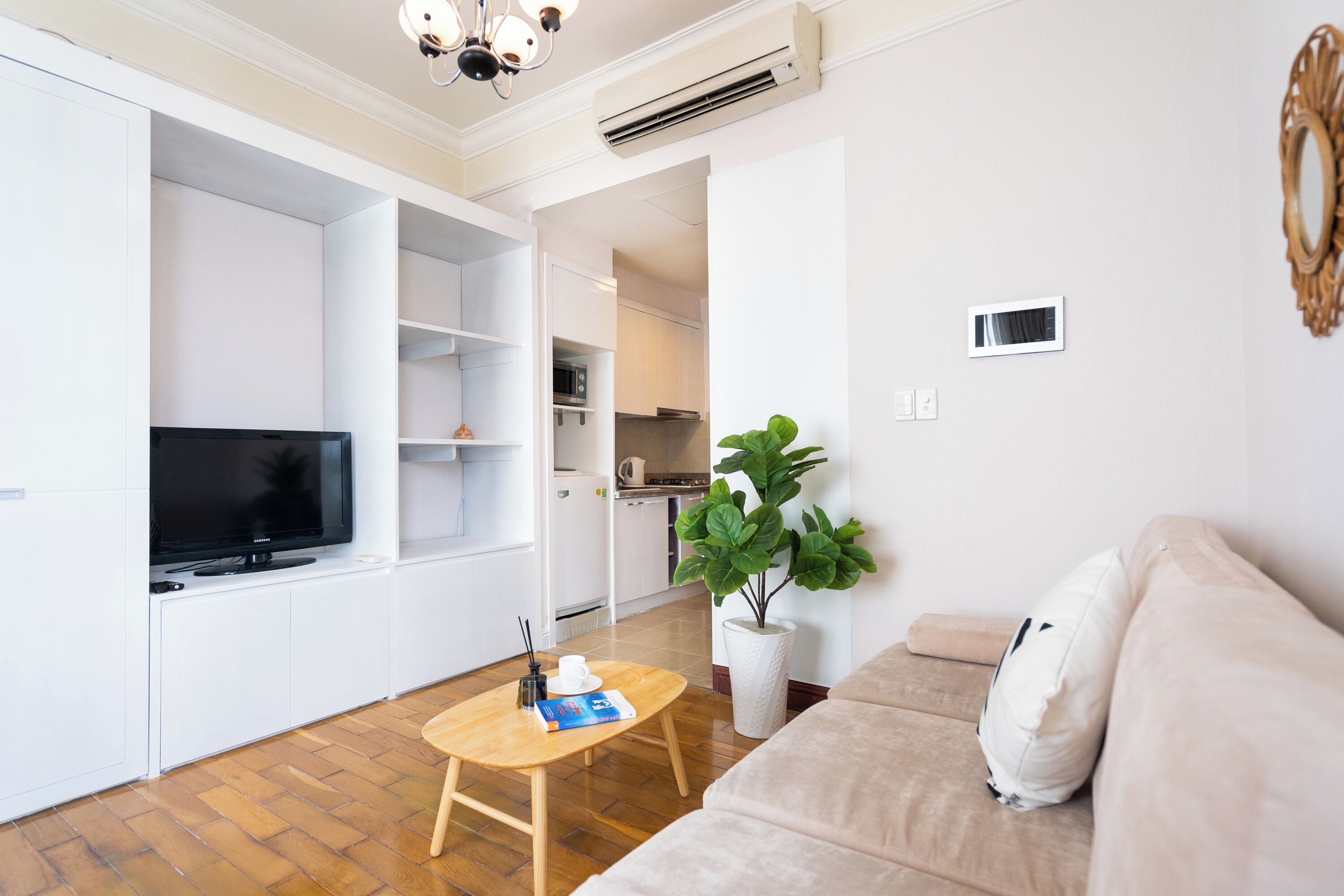 Una sala de estar moderna con televisor de pantalla plana, una mesa de centro de madera, un sofá color beige y una planta grande en maceta.