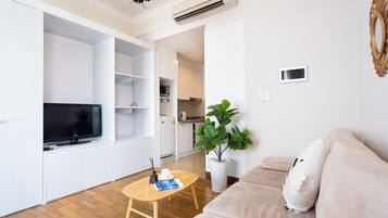 Una sala de estar moderna con televisor de pantalla plana, una mesa de centro de madera, un sofá color beige y una planta grande en maceta.