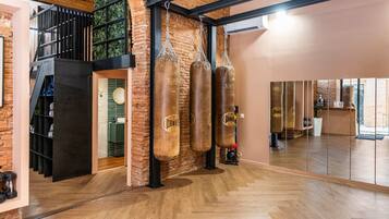 Una habitación amplia con suelo de madera, pared de ladrillo y tres sacos de boxeo colgados del techo.