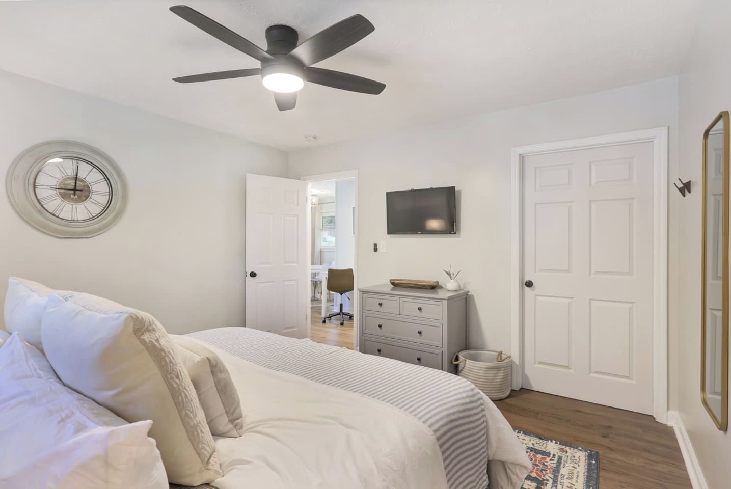 A bedroom with a bed, a dresser, a ceiling fan, a wall clock, and a television.