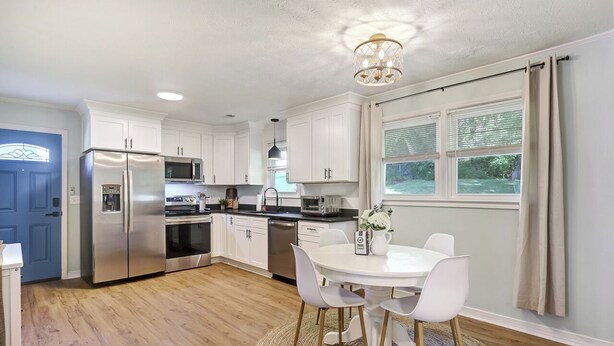 Una cocina moderna con armarios blancos, electrodomésticos de acero inoxidable y un comedor con mesa y sillas blancas.