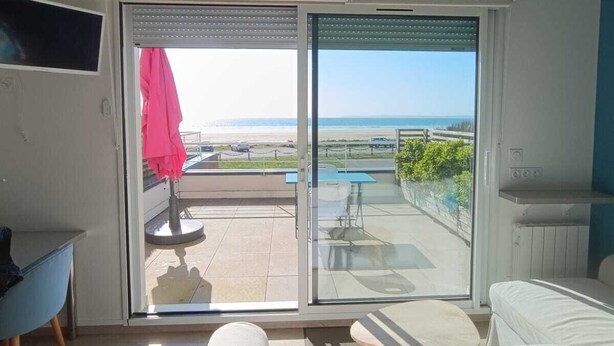 A living room with a sofa, a TV, and a sliding glass door leading to an outdoor area with a pool and a view of the beach. - New waterfront rental with sea view (Plomodiern)