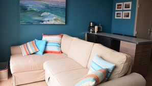 A living room with a beige sectional sofa, a coffee maker, and a painting of the ocean on the wall. - New waterfront rental with sea view (Plomodiern)