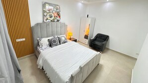 A modern bedroom with a bed, a chair, a wardrobe, and a painting on the wall. - The 401 Apartment (Tema)