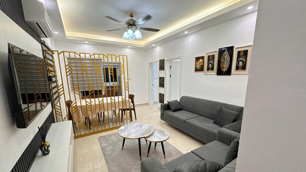 A modern living room with a grey sofa, a coffee table, and a dining area with a partition. - The 401 Apartment (Tema)