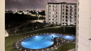 A swimming pool with a surrounding deck and lights, set against a backdrop of a cloudy sky and a multi-story building. - The 401 Apartment (Tema)
